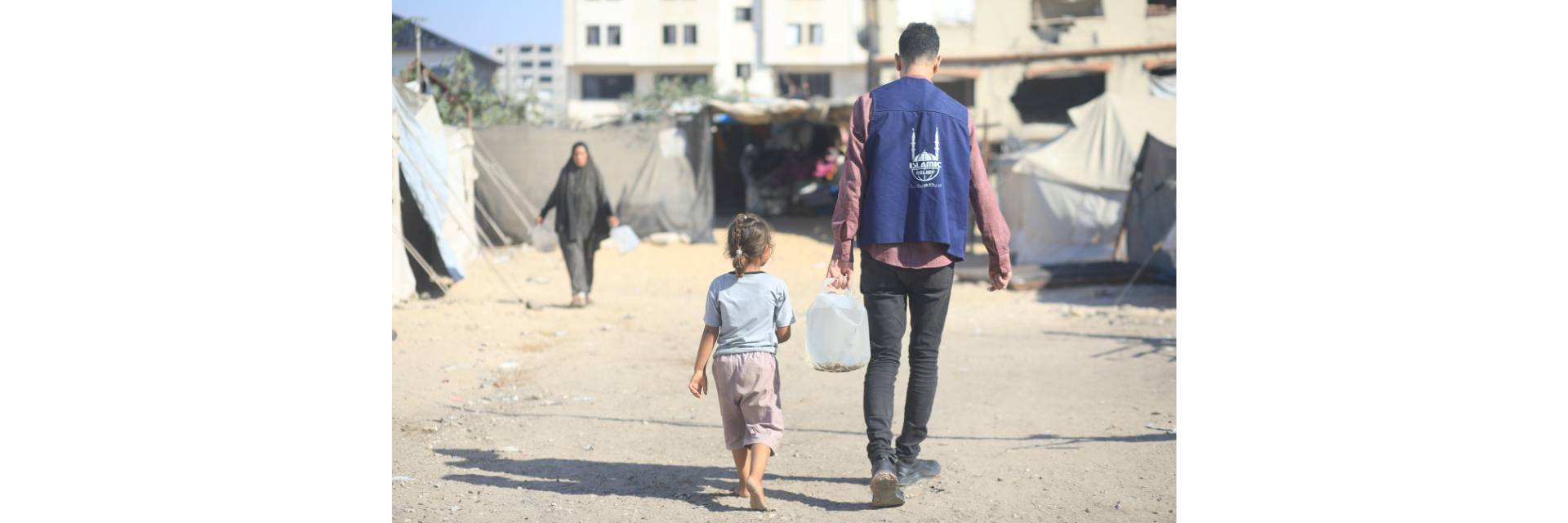 A humanitarian worker carries water for a child in a displacement camp