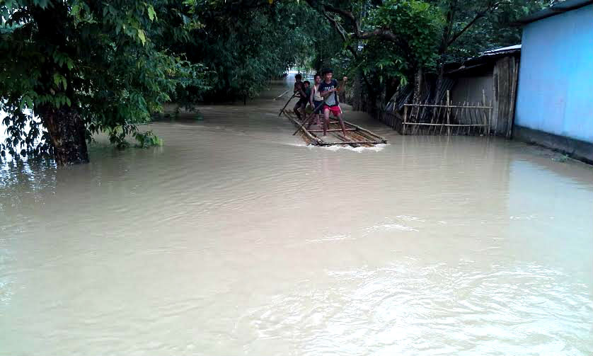 Four youth use poles to navigate through their flooded community in Assam, India 2016