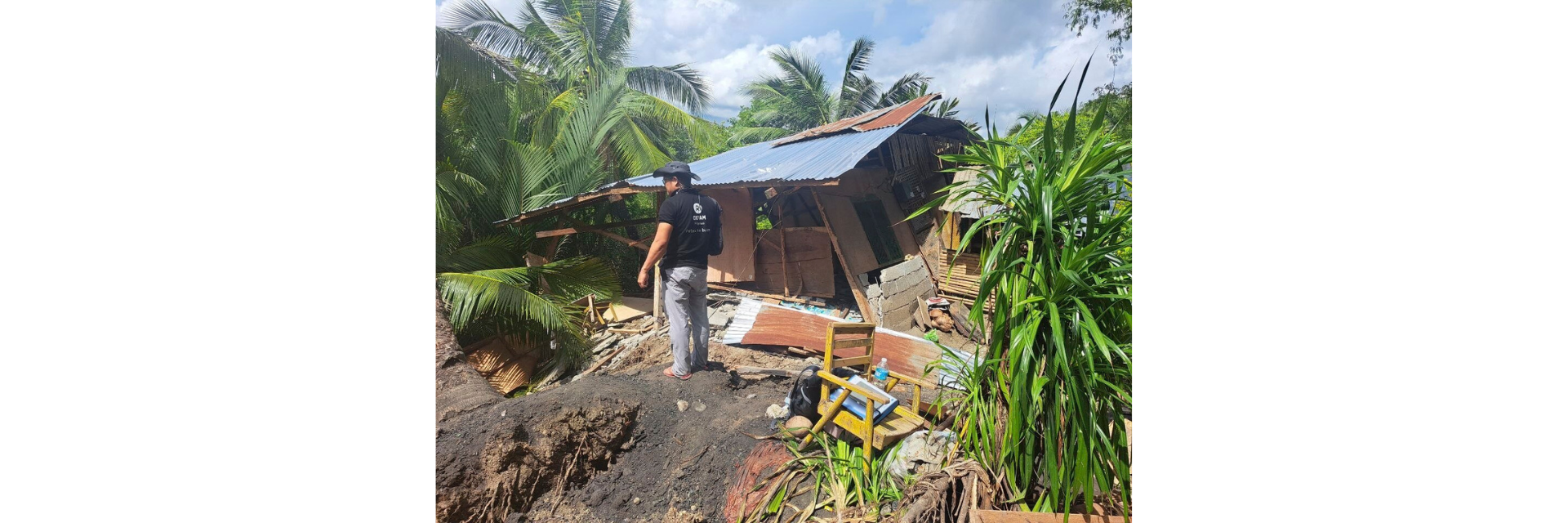 An Oxfam Philippines humanitarian worker surveys a severely damaged home surrounded by fallen debris.
