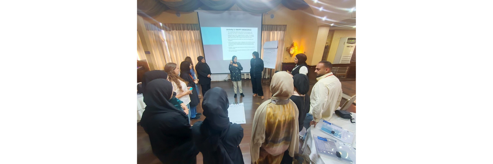 A group of people stand in a circle. A document on a projector reads "Activity one: Happy memories"