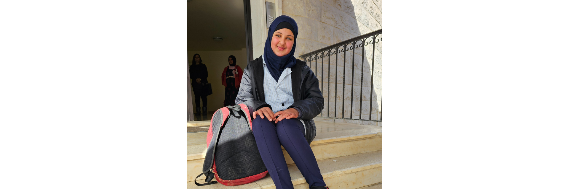 Lana on the steps of the education centre, with her mother Fatouma standing behind her.