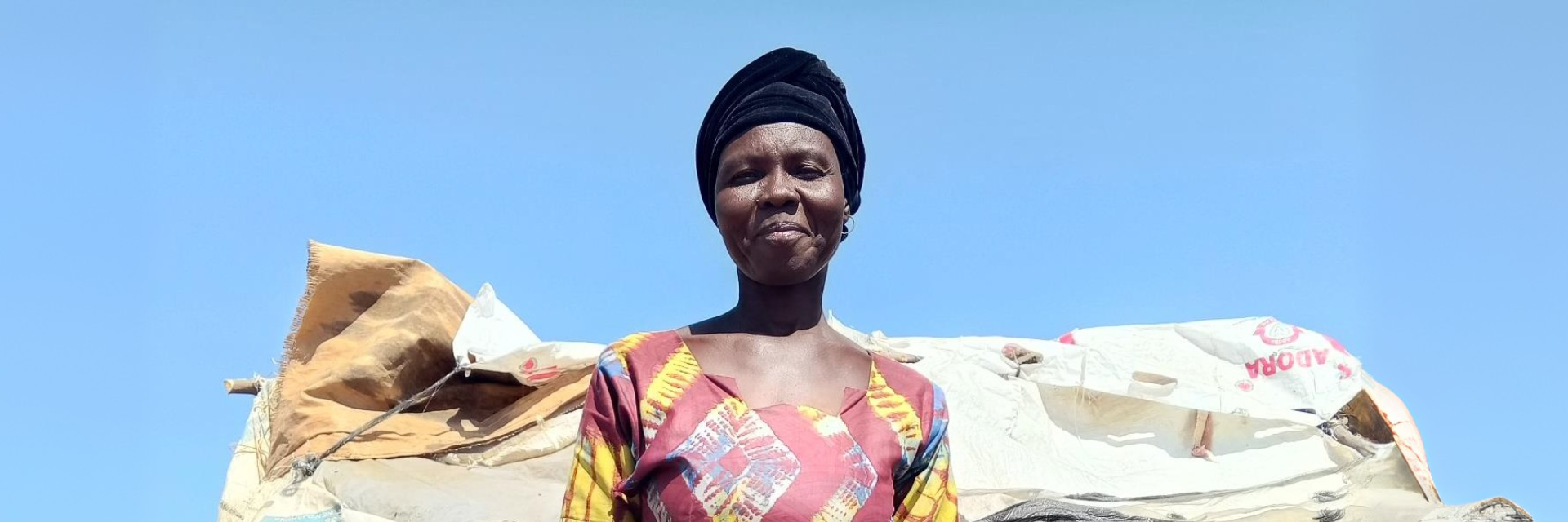 A woman in colourful clothing stands in front of a shelter