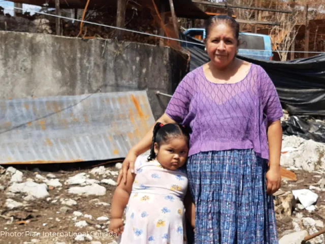 Geovana and her daughter in front of her ruined home