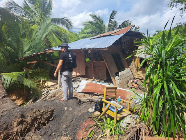 An Oxfam Philippines humanitarian worker surveys a severely damaged home surrounded by fallen debris.
