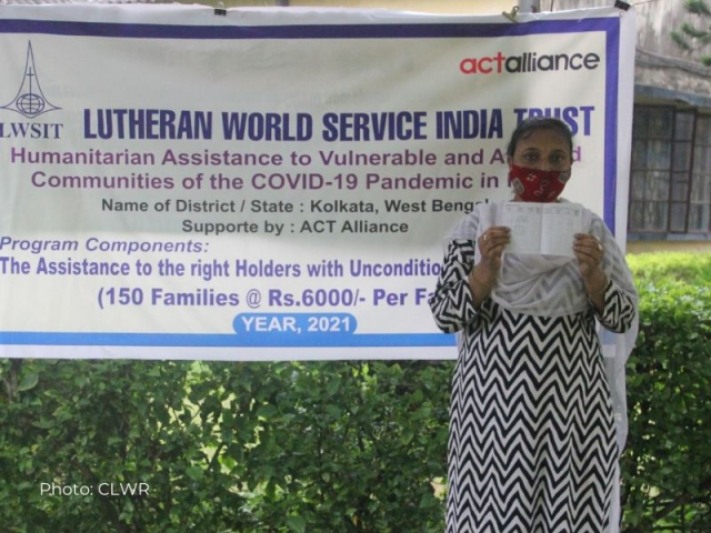 Shila Mondal stands in front of a program sign and shows her money transfer document
