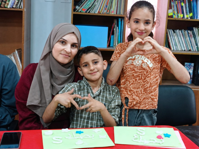 A mother and her two children making hearts with their hands while creating handmade cards at the Makani Club.