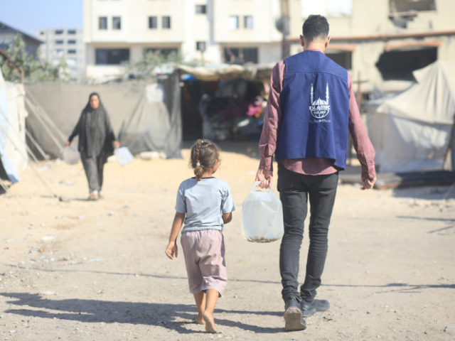 A humanitarian worker carries water for a child in a displacement camp