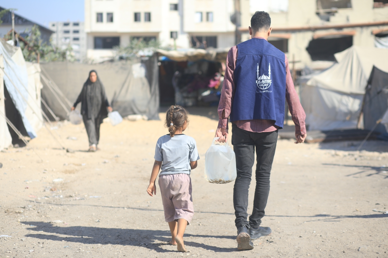 A humanitarian worker carries water for a child in a displacement camp